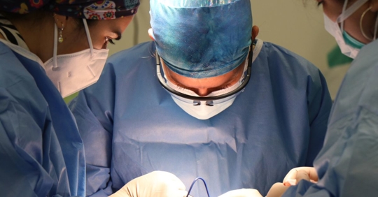 group of three people wearing hospital scrubs and masks looking down on a surgical table