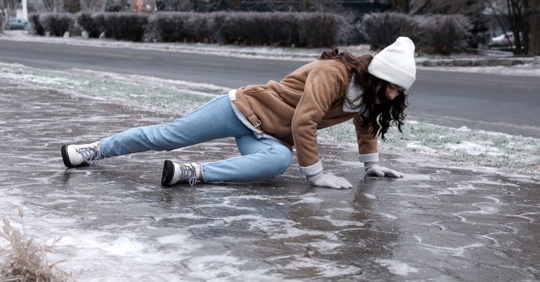 Young woman trying to stand up after falling on slippery icy pavement outdoors